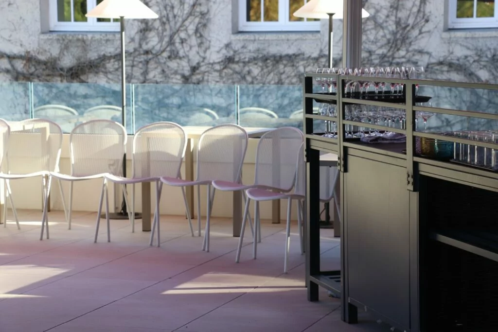 La terrasse dressée pour un cocktail, chaises blanches et verres alignés sur le bar